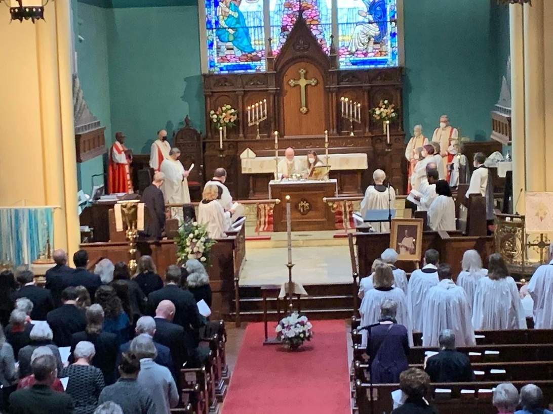 Interiör av en kyrka under en begravningsgudstjänst, med präster vid altaret och sörjande i bänkarna.